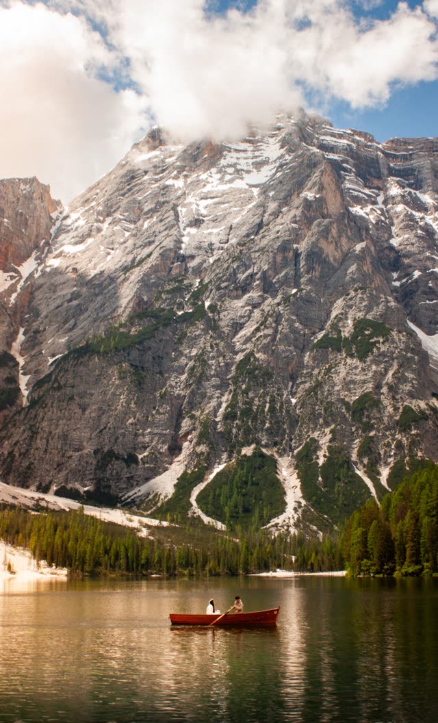 A snowy peak above a green lake, a red rowboat with two people on the water