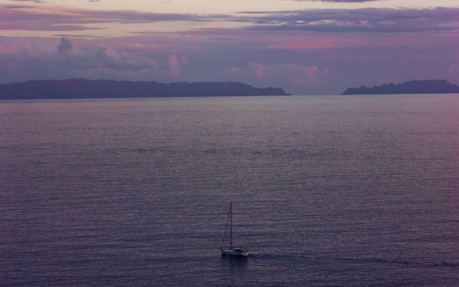 A lone sailboat on a purple sea at dusk, two islands on the horizon