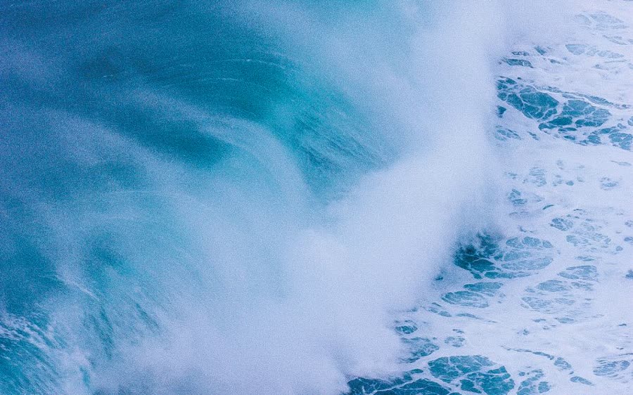 A turquoise wave breaking into white foam, seen from above