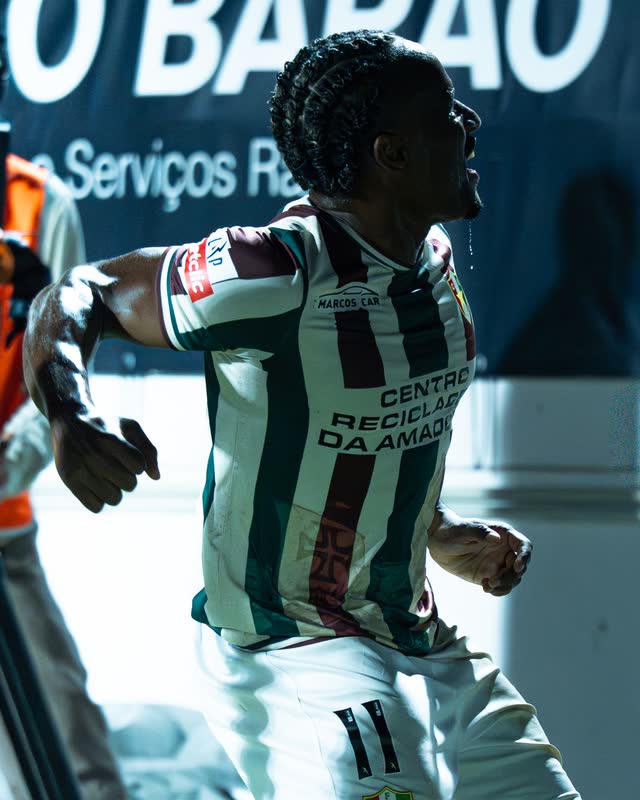 A player in a striped red, green and white kit roars, head thrown back, arms swinging