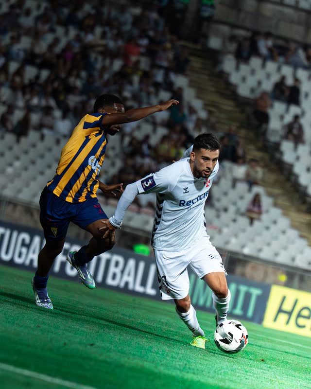 A winger in white runs with the ball, chased by a defender in yellow and blue