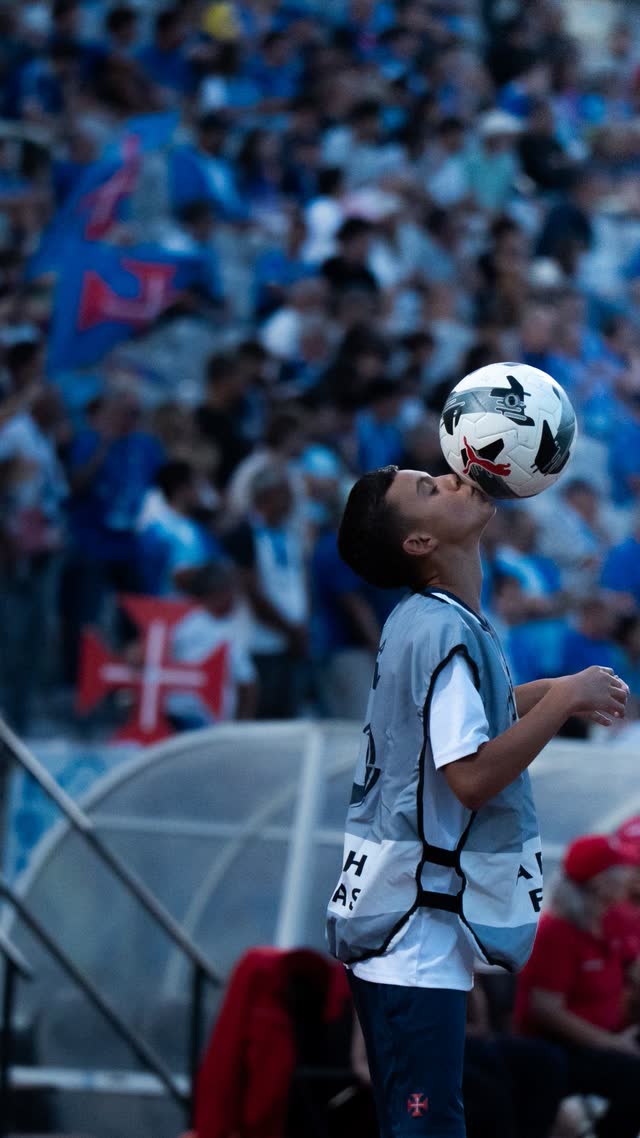 A ball boy balances the match ball on his face in front of a crowd in blue